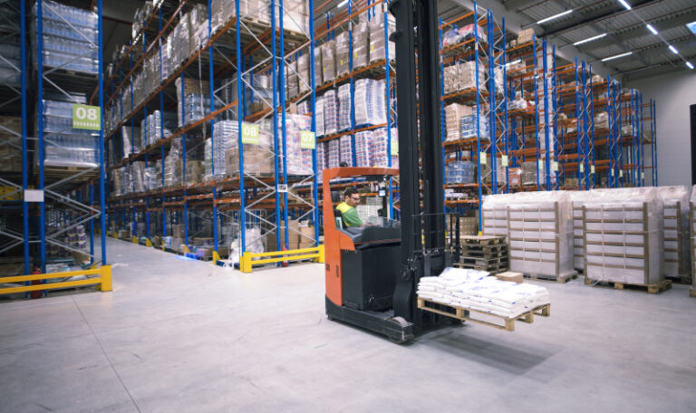Worker operating forklift machine and relocating goods in large